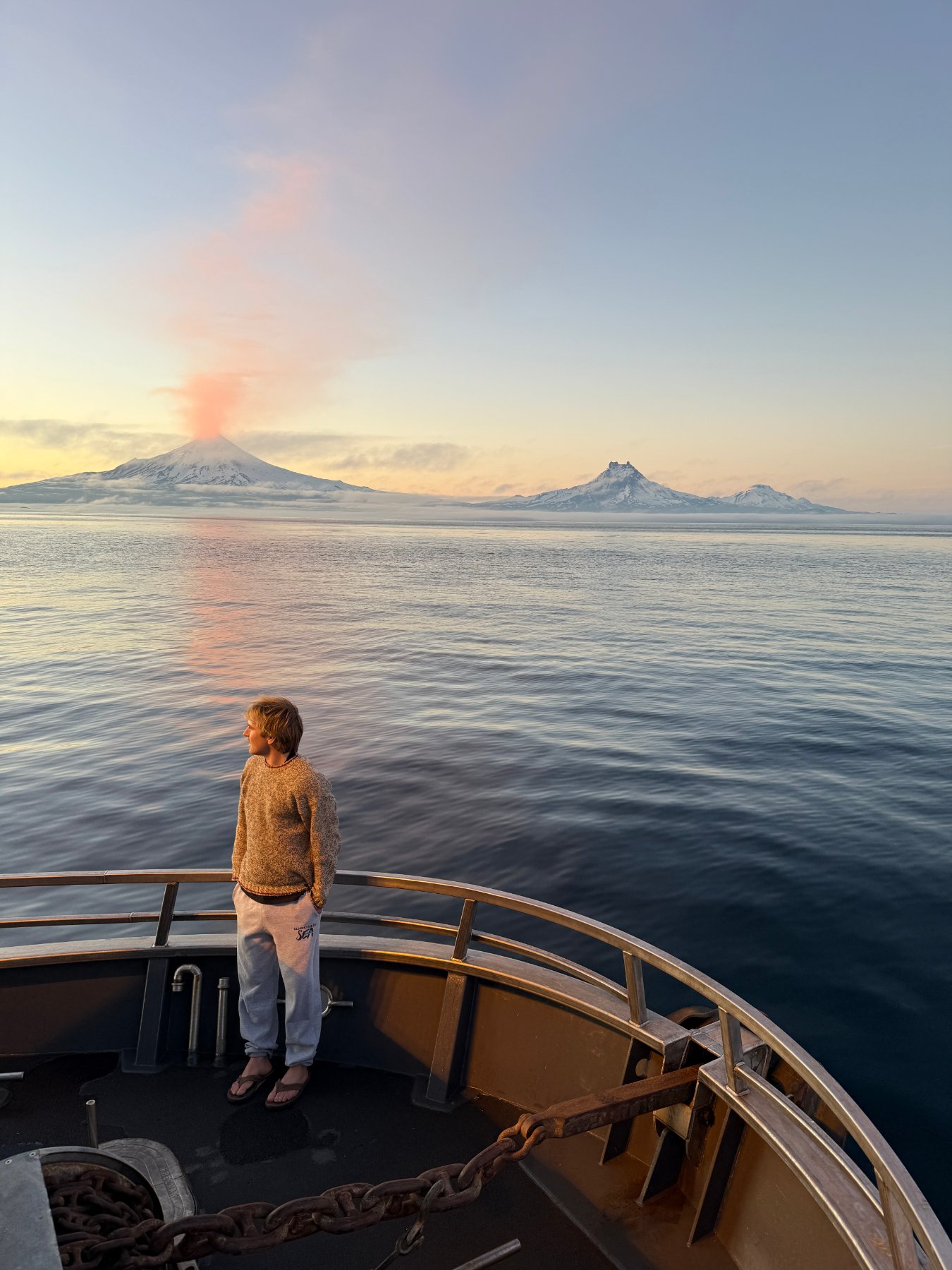 Calm water at sunset with a snow-capped volcano venting on the horizon