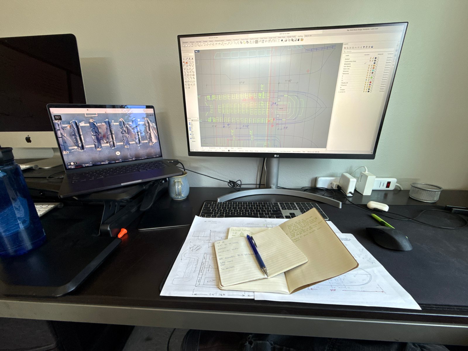 Desk with laptop and monitor, printed drawings and notes laid out