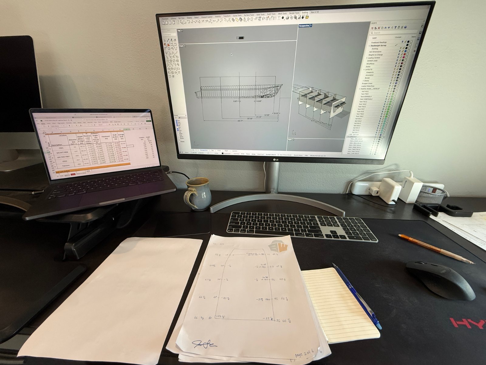 Monitor showing a 3D boat model in Rhino, paper drawings on the desk