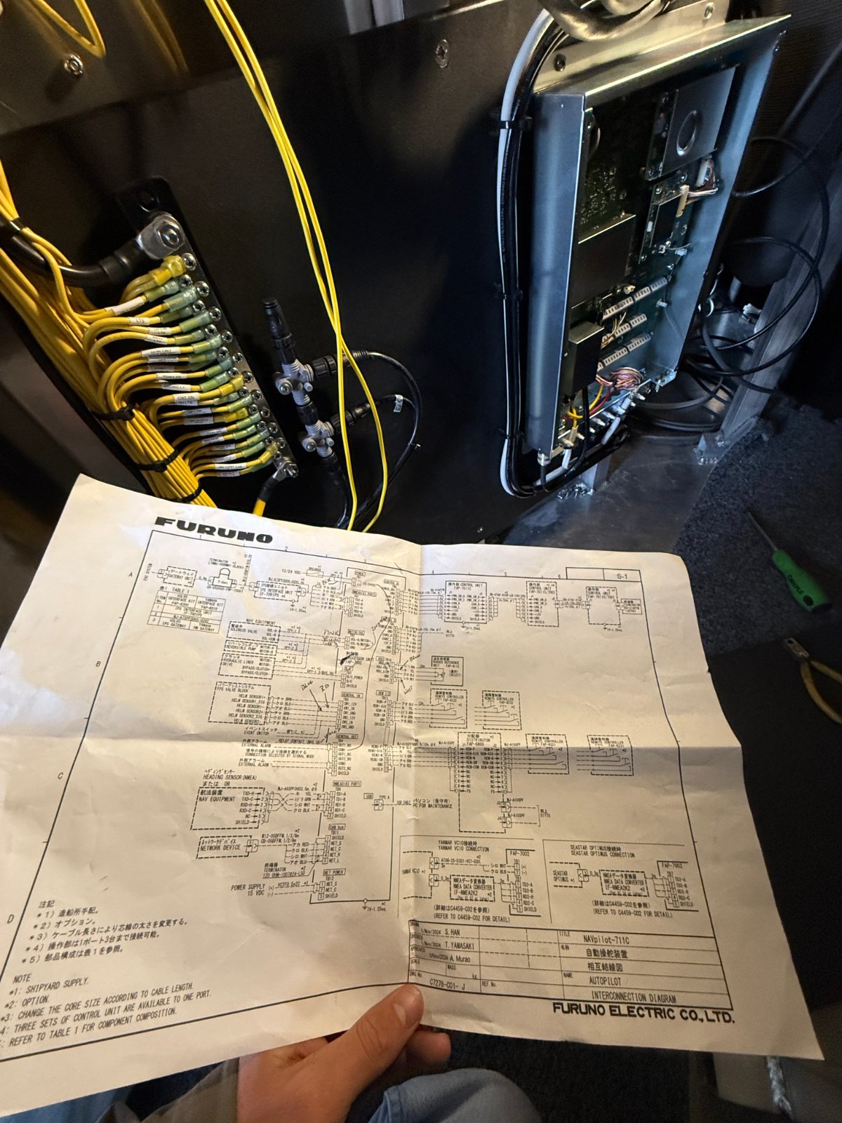 Printed schematic held up beside an open electrical panel